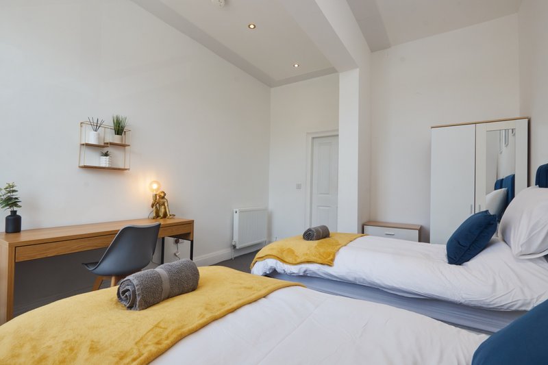 Modern bedroom with two beds, yellow bedding, wooden desk and white wardrobes