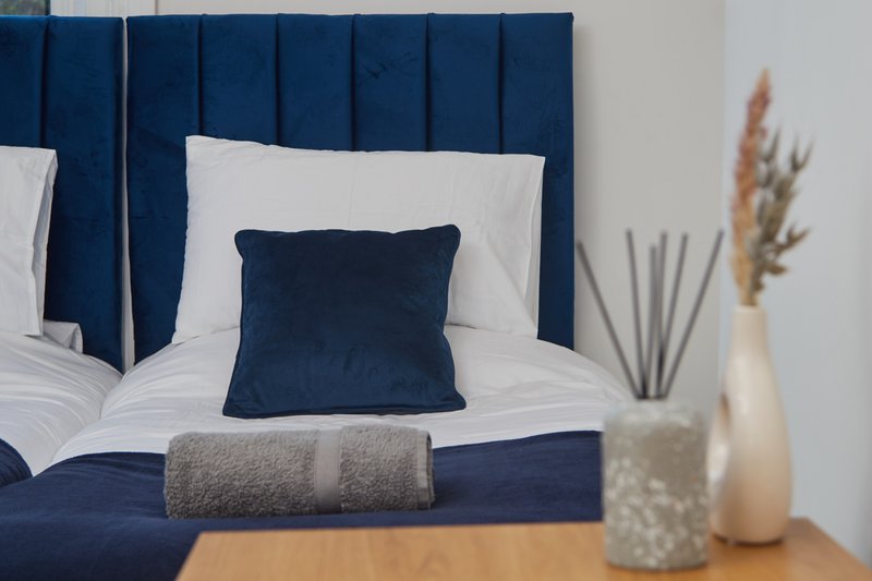 Modern bedroom with navy upholstered headboard, white bedding, dark cushion, and decorative vases on nightstand