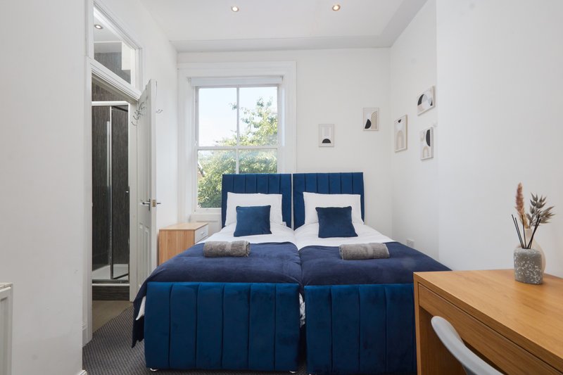 Bright bedroom with twin beds, blue headboards, wooden desk and garden view