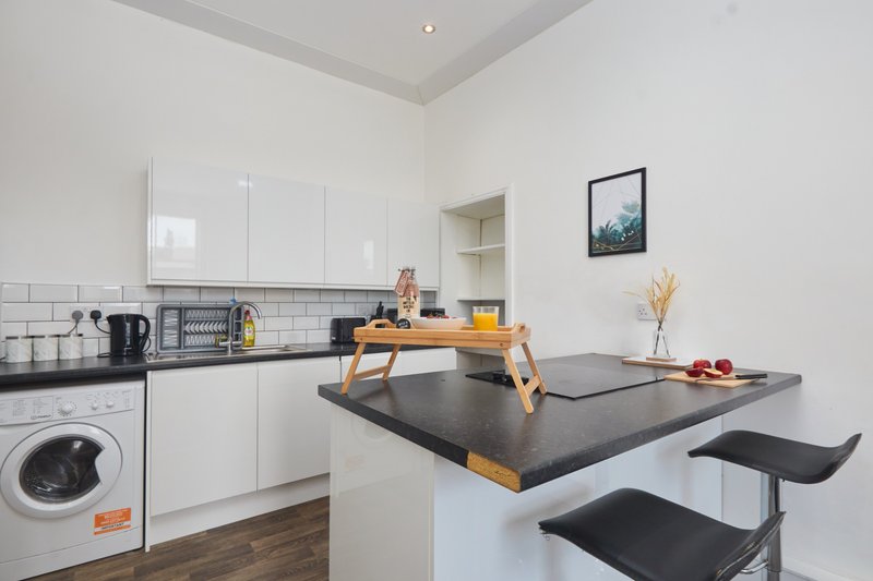 Modern white kitchen with black countertop, island seating, washing machine and wooden breakfast bar