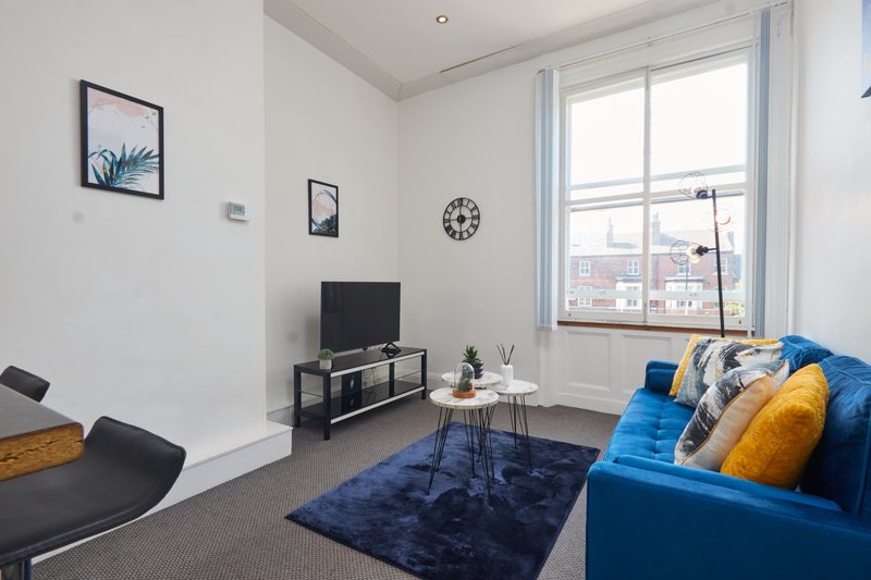 Modern living room with blue sofa, TV stand, wall art, and city views from large windows
