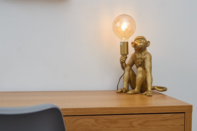 Wooden desk with decorative gold monkey lamp holding illuminated bulb