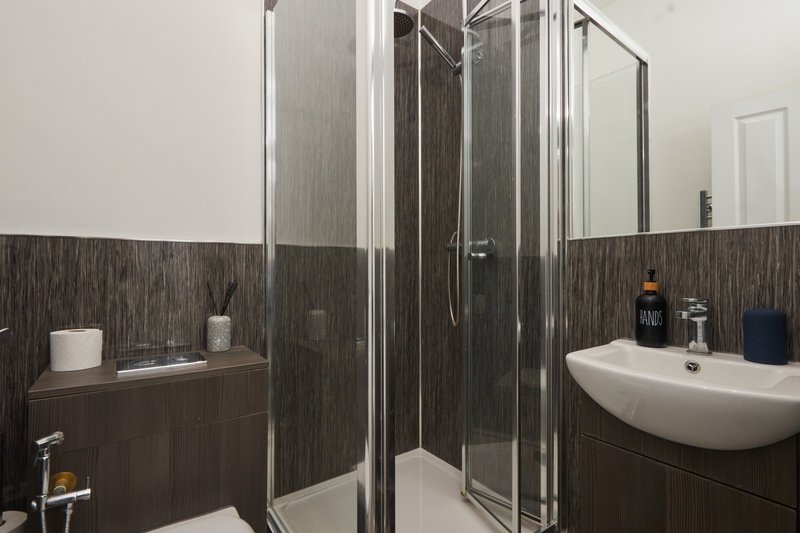 Modern bathroom with dark tile walls, shower enclosure, white sink and toilet