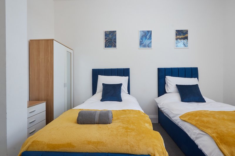 Twin bedroom with yellow bedspreads, blue headboards, white pillows, and wall art