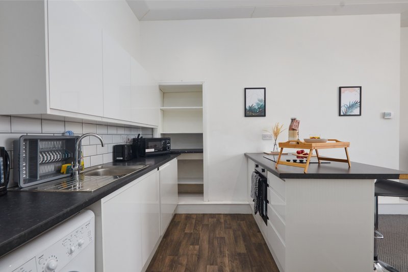 Modern kitchen with white cabinetry, black countertops, wooden flooring and island