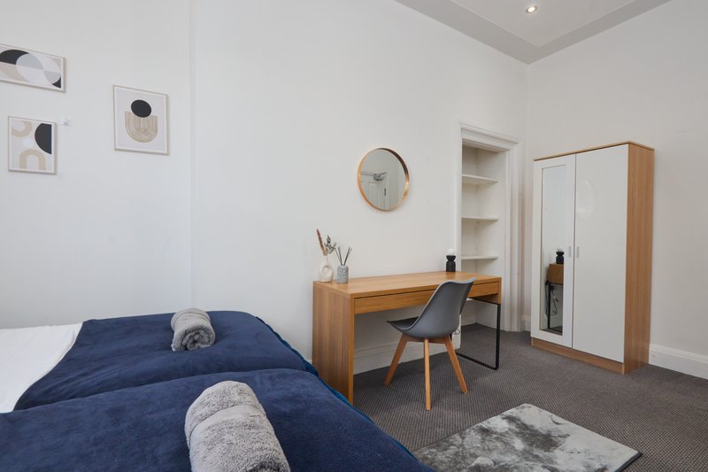 Modern bedroom with navy bed, wooden desk, chair, wardrobe and wall art
