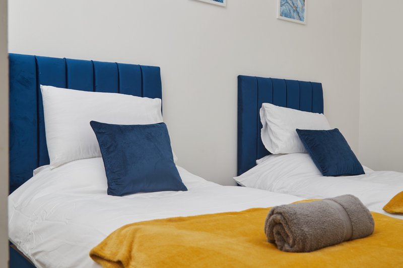 Twin bedroom with blue upholstered headboards, white bedding, navy cushions and yellow throw blankets