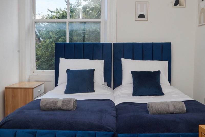 Bright bedroom with twin beds, navy blue headboards, white linens, and large window overlooking garden