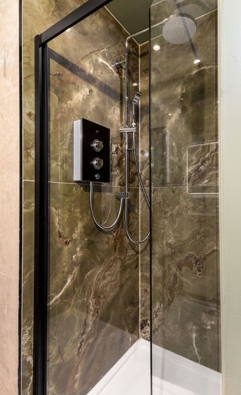 Modern bathroom shower enclosure with black frame, marble-effect tiles and rainfall showerhead