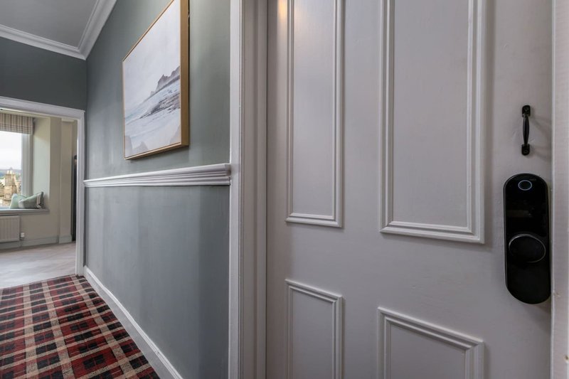 Hallway with gray paneled walls, framed artwork, patterned runner carpet and door