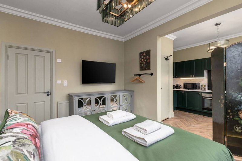 Bedroom with double bed, green throw, white cabinet headboard, wall-mounted TV and ensuite bathroom visible