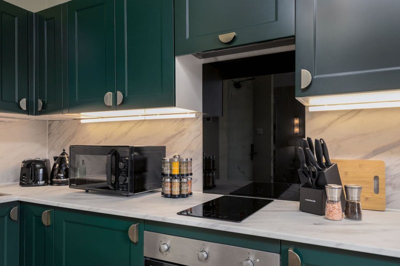 Modern kitchen with dark green cabinetry, white marble countertop, black appliances and utensil storage