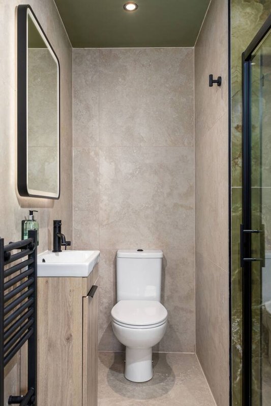 Modern bathroom with toilet, white sink, framed mirror and tiled walls