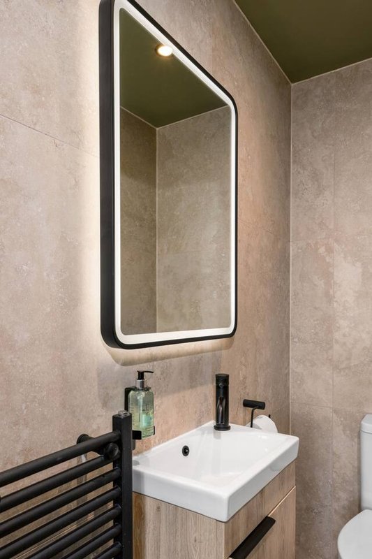 Modern bathroom with illuminated mirror, white sink, wooden vanity and black towel rail