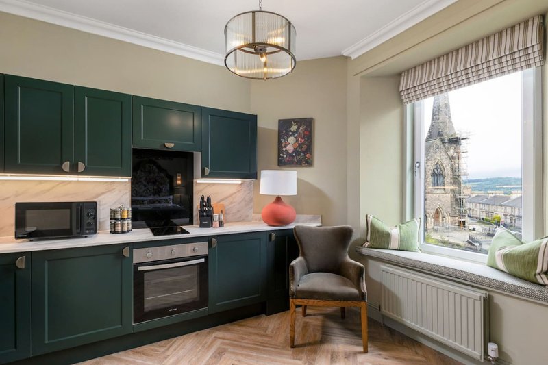 Modern kitchen with dark green cabinets, wooden worktop, and window seat overlooking cityscape