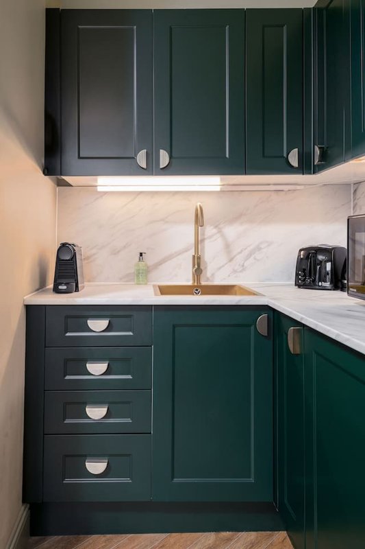Modern kitchen with dark green cabinetry, marble backsplash, brass faucet and white countertop
