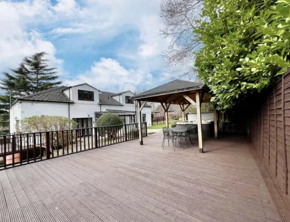 Spacious composite decking with black railings, pergola, and modern house with garden beyond