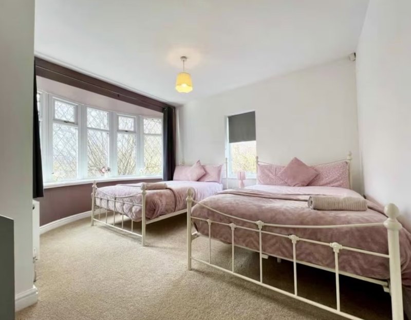 Bright bedroom with two single beds, pink bedding, large window and yellow ceiling light