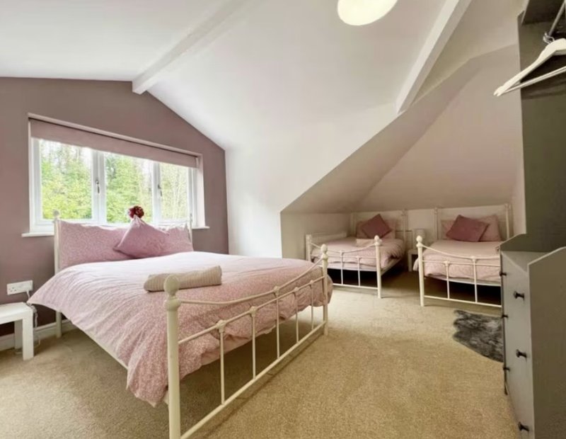 Spacious attic bedroom with pitched ceiling, pink bedding, metal bed frame and twin beds