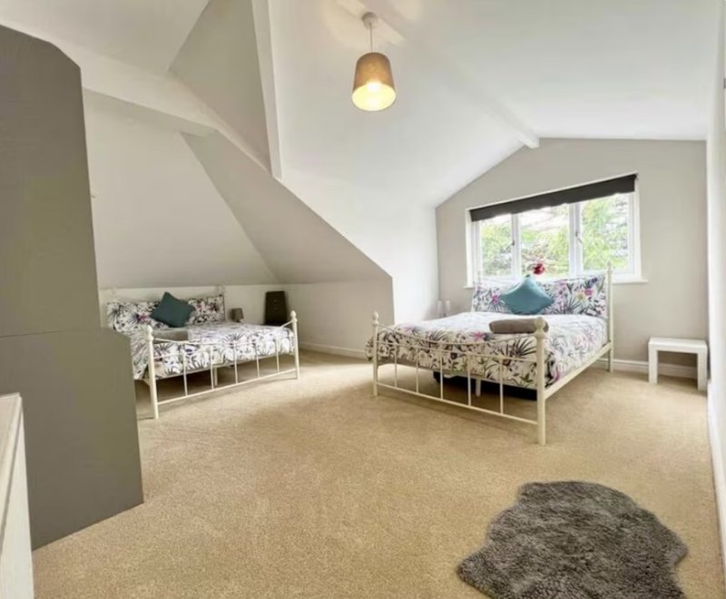 Bright attic bedroom with two single beds, sloped ceiling, pendant light, and carpet flooring