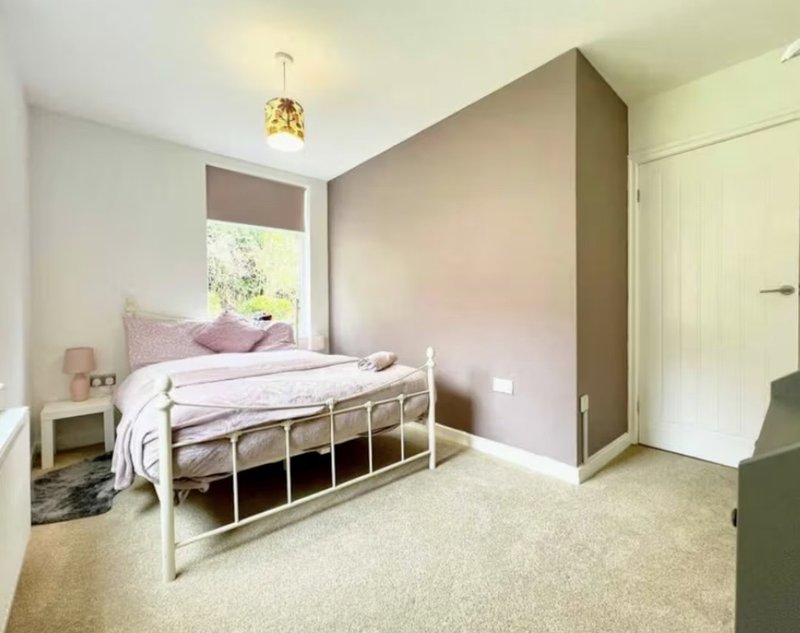 Bedroom with white metal bed frame, pink bedding, built-in wardrobe and window