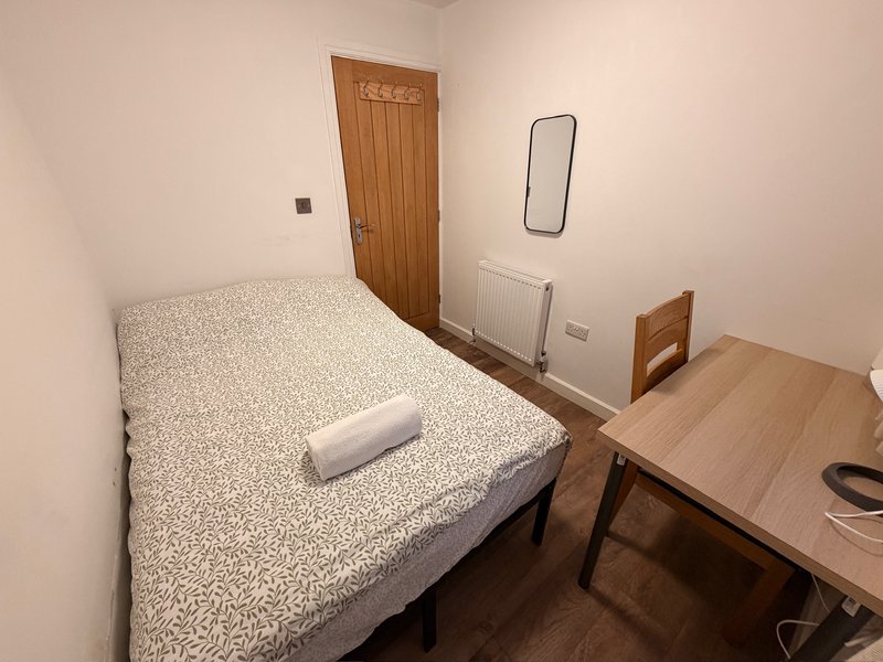 Small bedroom with single bed, wooden door, desk, chair and radiator