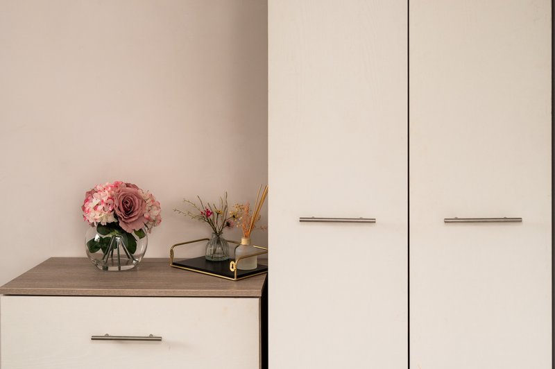 Modern bedroom with white cabinetry, wooden shelf, pink flowers in vase, and minimal decor