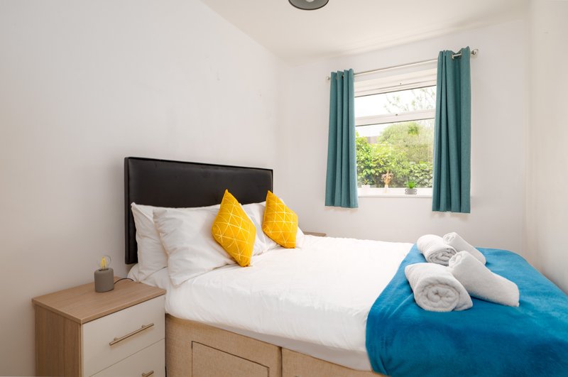 Bright bedroom with double bed, yellow cushions, wooden nightstand, and blue throw blanket