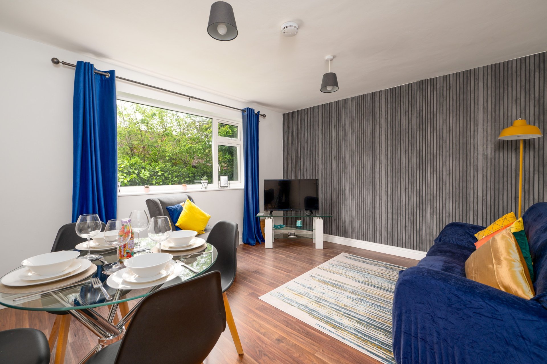 Open-plan living and dining area with blue curtains, dining table, sofa, and garden view