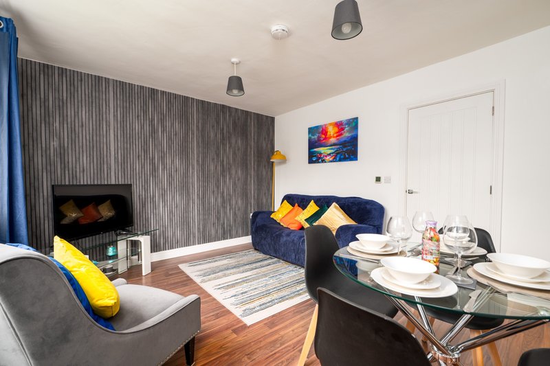 Modern open-plan living room with blue sofa, dining table, fireplace and yellow accent cushions