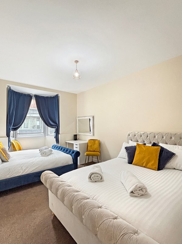 Bright twin bedroom with two beds, blue curtains, yellow accents, and pendant light