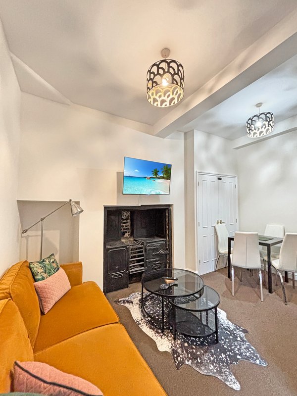 Living room with yellow sofa, fireplace, TV on mantle, dining area and modern ceiling lights