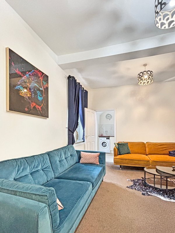 Open-plan living room with turquoise and orange sofas, abstract wall art, and stacked appliances