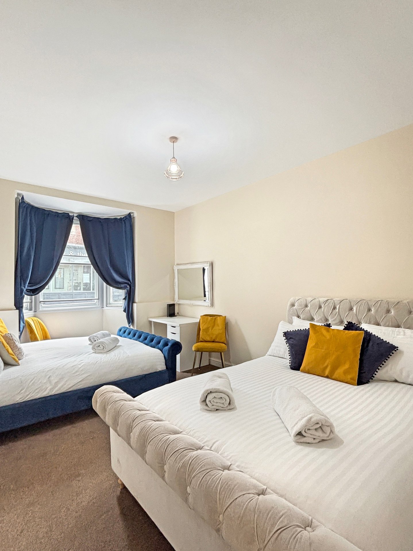 Bright twin bedroom with white beds, blue curtains, yellow accent pillows and chair