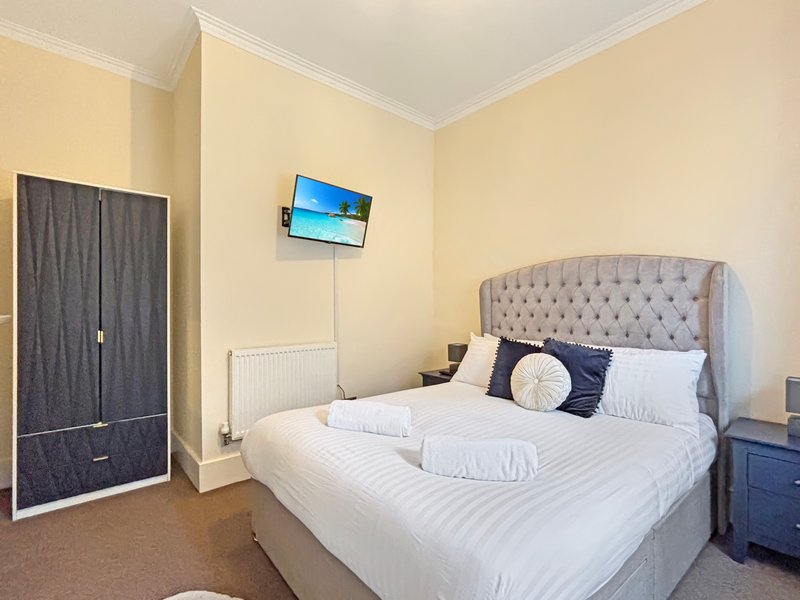 Bedroom with double bed, upholstered headboard, wall-mounted TV, wardrobe and bedside tables