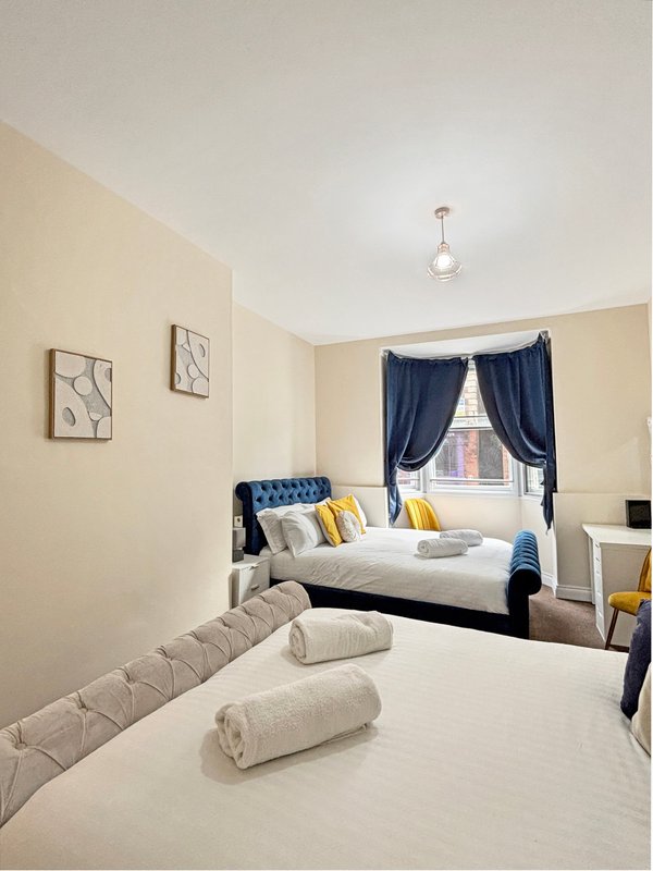 Bright bedroom with two beds, yellow and blue cushions, pendant light and framed wall art
