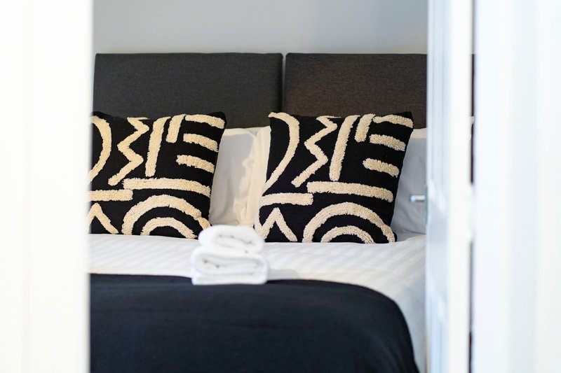 Bedroom with dark headboard, patterned cushions, white pillow and navy bedding