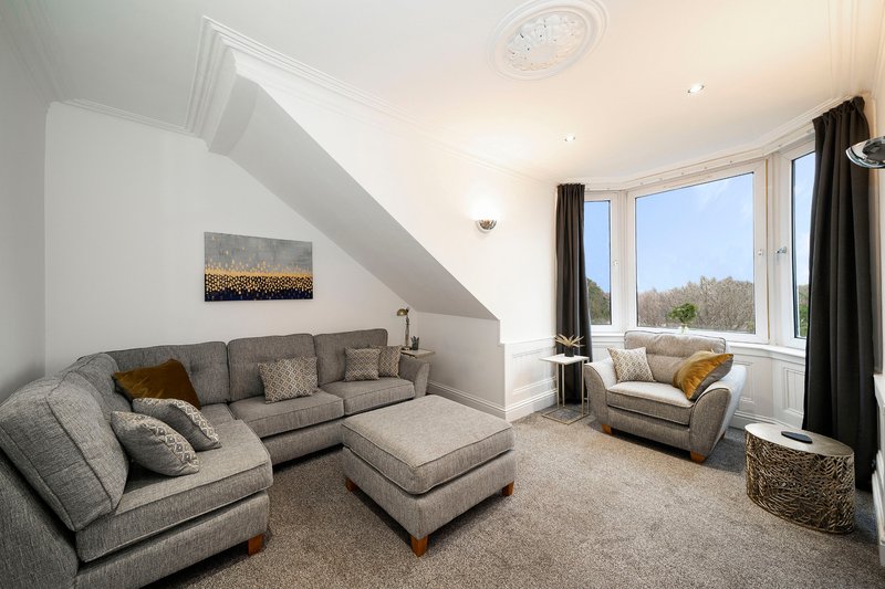 Bright attic living room with grey corner sofa, armchair, and large windows overlooking trees