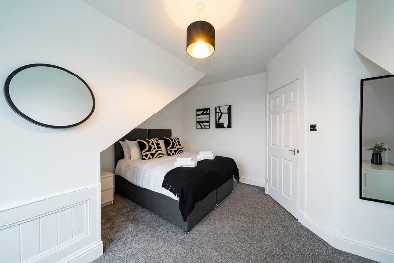 Modern bedroom with single bed, grey carpet, round mirror and ceiling light