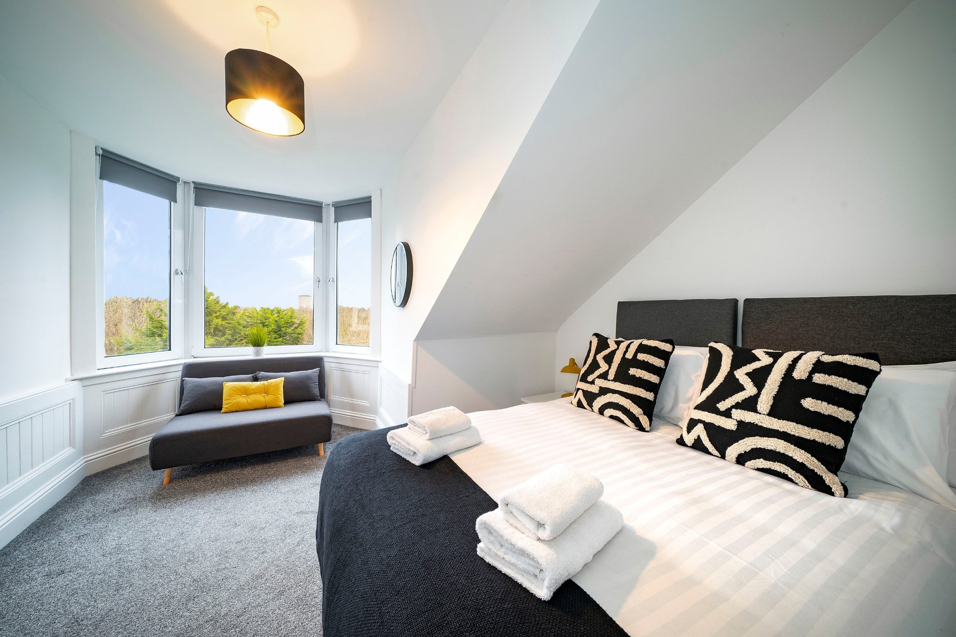 Bright attic bedroom with double bed, zebra-patterned cushions, window seat and ceiling light