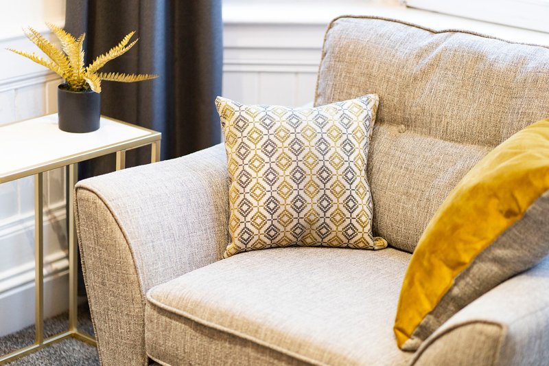 Modern living room armchair with patterned cushions and side table with decorative vase