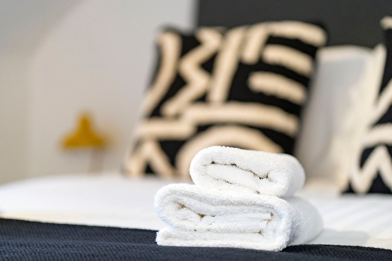 Rolled white towels on bed with geometric patterned pillows in background