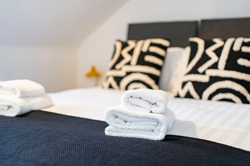 Bedroom with neatly folded white towels on bed, patterned pillows and headboard