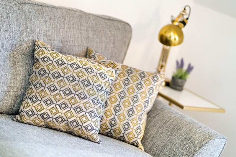 Grey sofa with patterned cushions, brass floor lamp and small potted plant