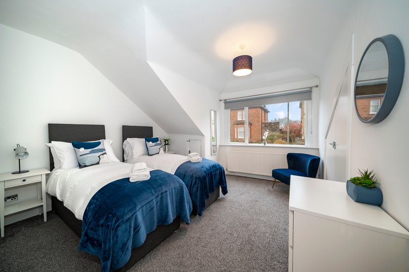 Bright attic bedroom with two single beds, blue bedding, white walls and round mirror
