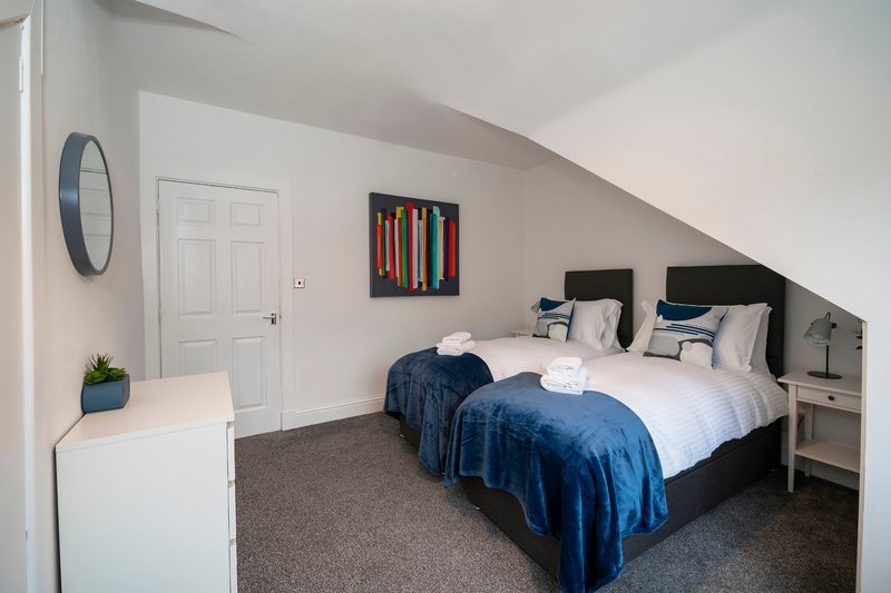 Bright attic bedroom with twin beds, blue bedding, white door and wall-mounted clock