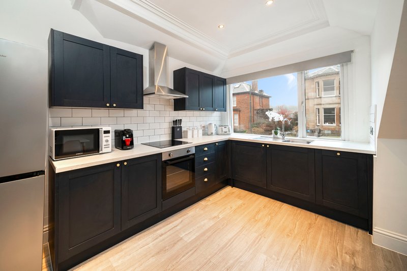 Modern kitchen with black cabinetry, white subway tile backsplash, wooden flooring and window view