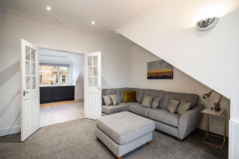Bright attic living room with gray L-shaped sofa, ottoman, and abstract wall art