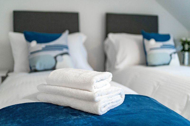 Twin bedroom with folded white towels on blue bedding, modern headboards and pillows