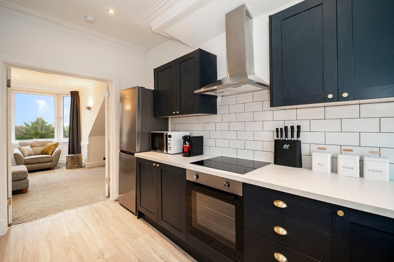 Modern kitchen with black cabinetry, white subway tile backsplash, stainless steel appliances and open door to living area
